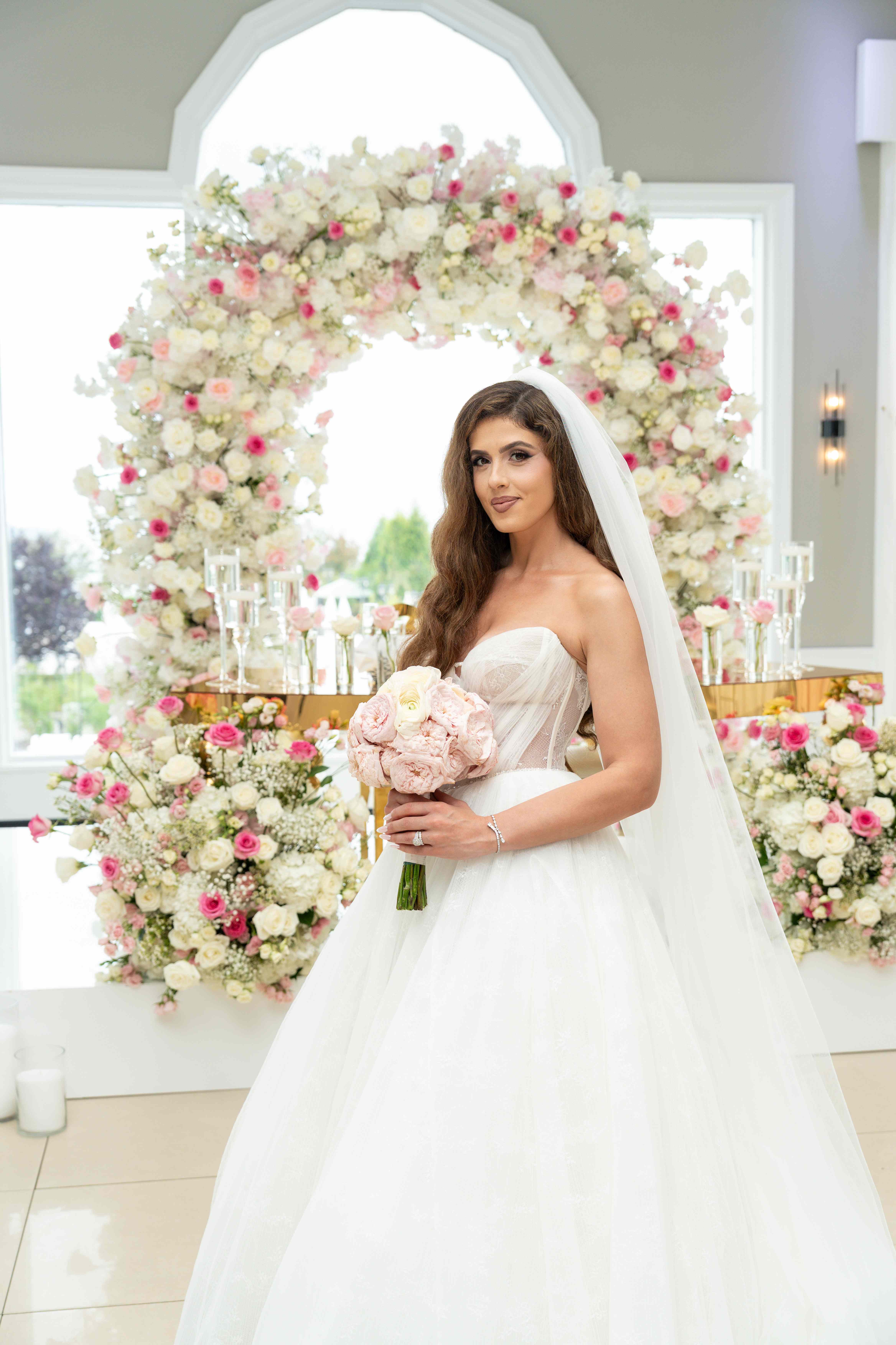 Beautiful bride with bouquet in front of elegant floral ceremony arch