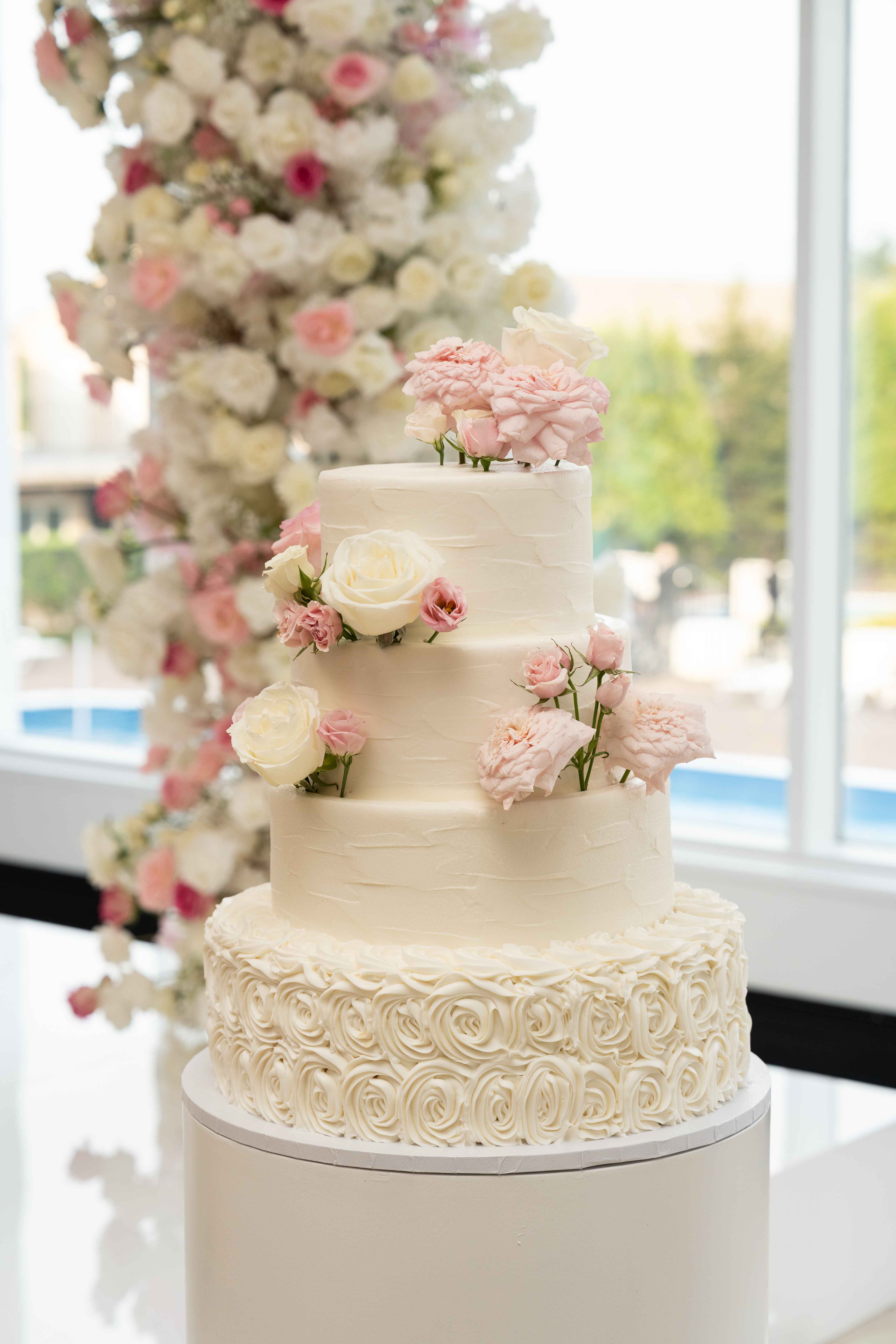 Elegant white wedding cake with fresh pink roses and tall floral centerpiece